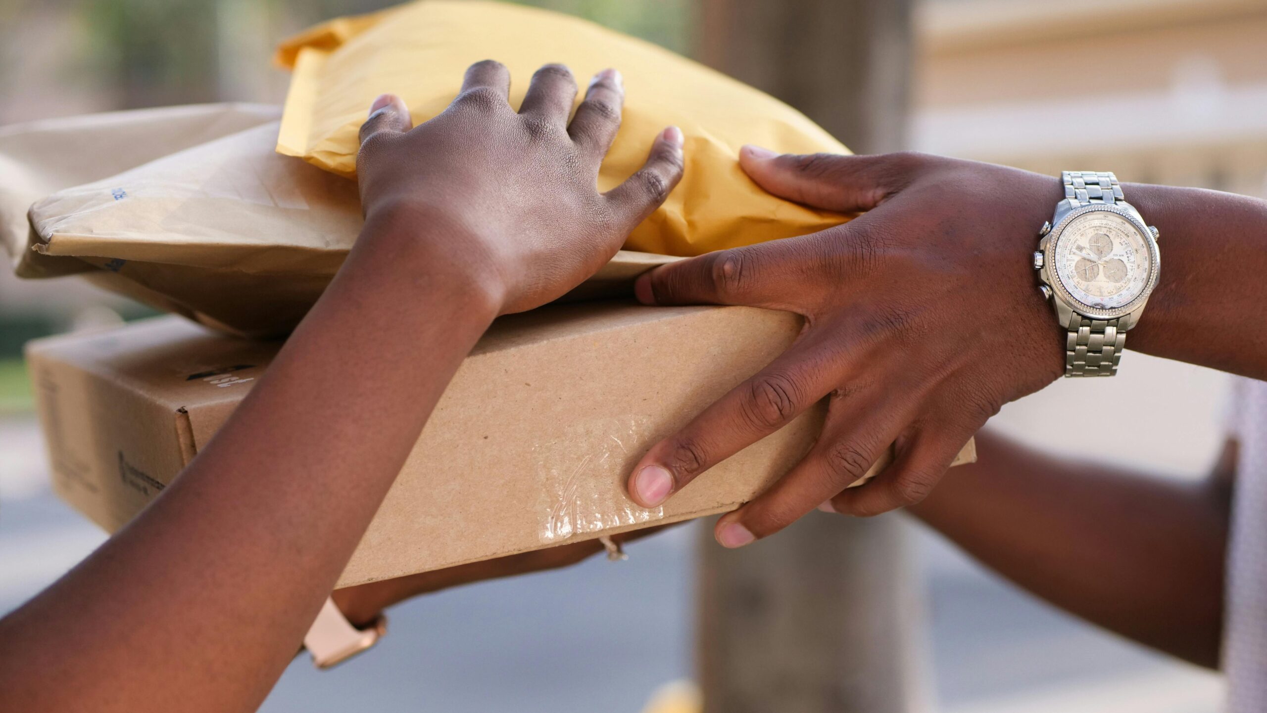 Picture of woman's hands receiving a package delivery from the hands of a man. 