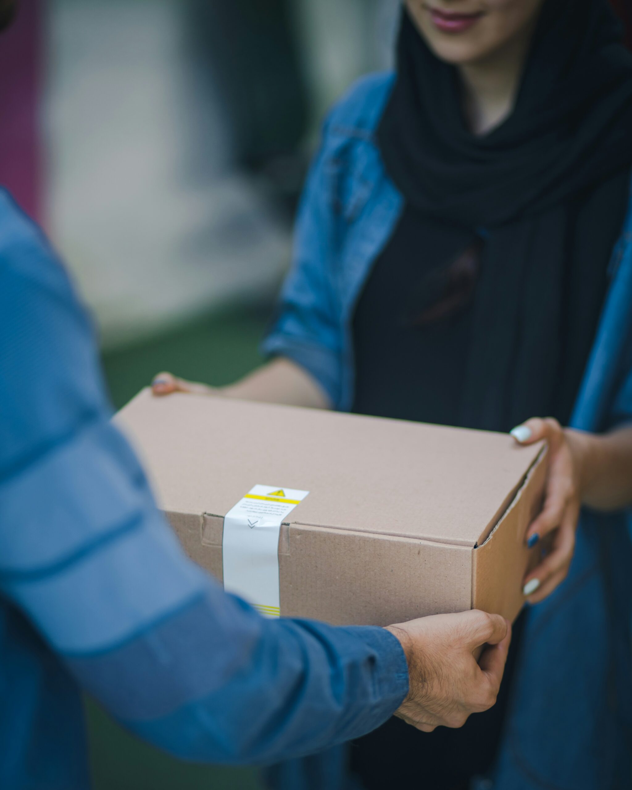 Picture of woman's hands receiving a package delivery from the hands of a man. 