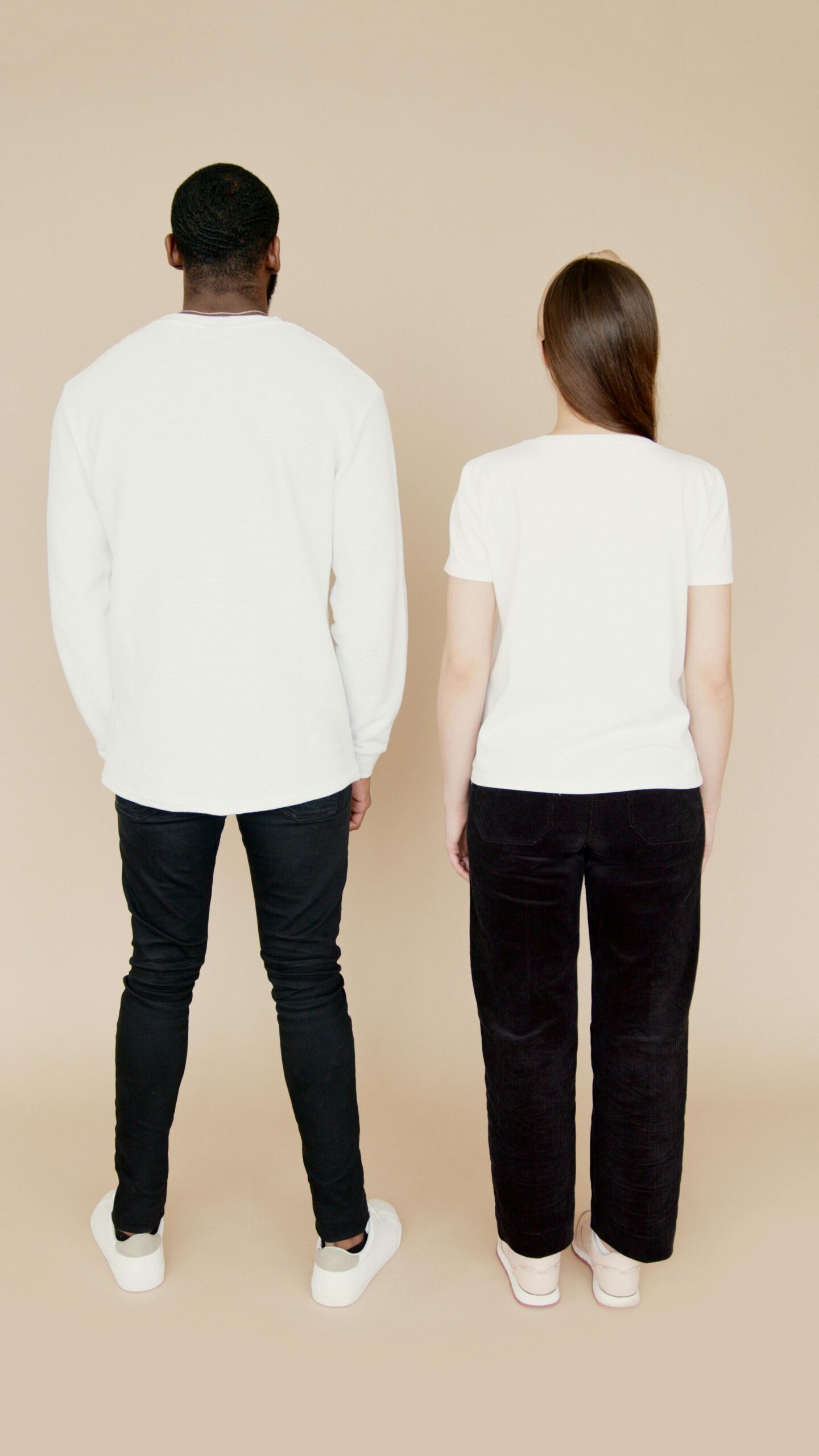 A diverse couple stands back to camera in casual white shirts, perfect for fashion concepts.